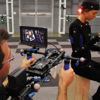 A man filming an actress that is wearing a body suit with motion sensors attached to it.