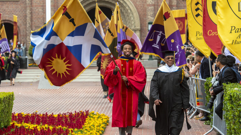 USC graduates carrying flags for their respective schools on commencement