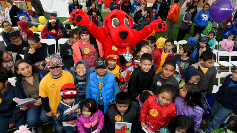 Children posing for a picture with an individual in a Clifford the big red dog costume