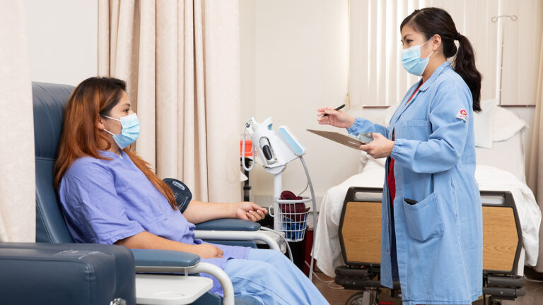 Nurse speaks to patient as they use a machine to check blood pressure.