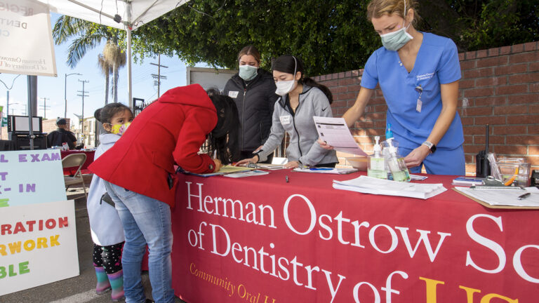 Mother registers child at table for Herman Ostrow School of Dentistry of USC's mobile clinic event.