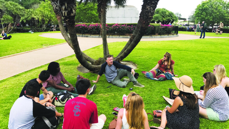 Students sit in a circle on a grass lawn on USC's campus.