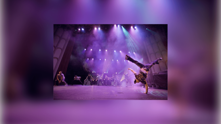 A member of the breakdance troupe dancing, doing a one-hand stand