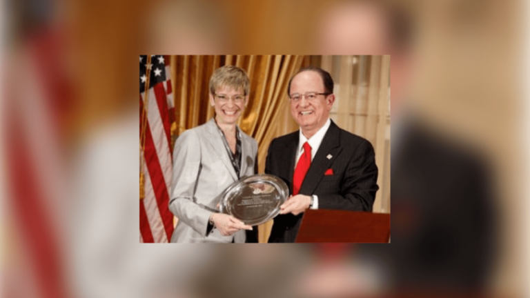Provost Garrett, a white woman with short blonde hair and glasses and a gray suit, smiling next to President Nikias, a white man with glasses and a black suit and red necktie.