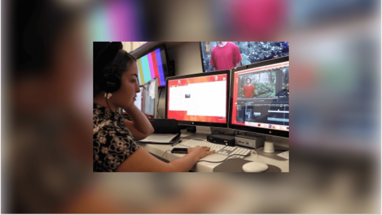 A female student working with headphones at a dual monitor, editing a video.