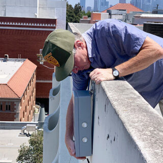 A man fixing a box on the side of a building.