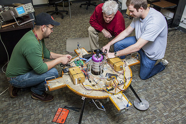 USC Viterbi School of Engineering students sitting on the floor work on an engineering project with a faculty member.
