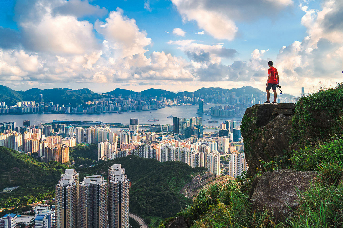A man standing on the edge of a cliff overlooking a city.