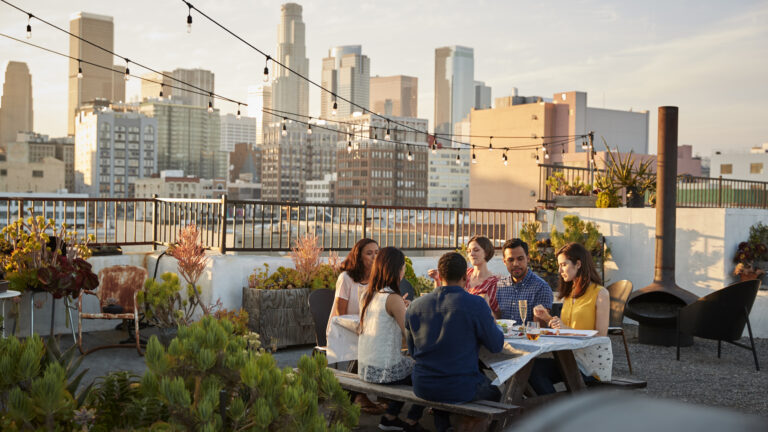 Friends Gathered On Rooftop Terrace For Meal With City Skyline In Background in Los Angeles.