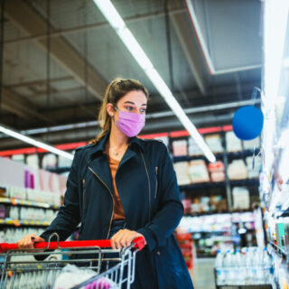 Woman with face mask pushing shopping cart in supermarket